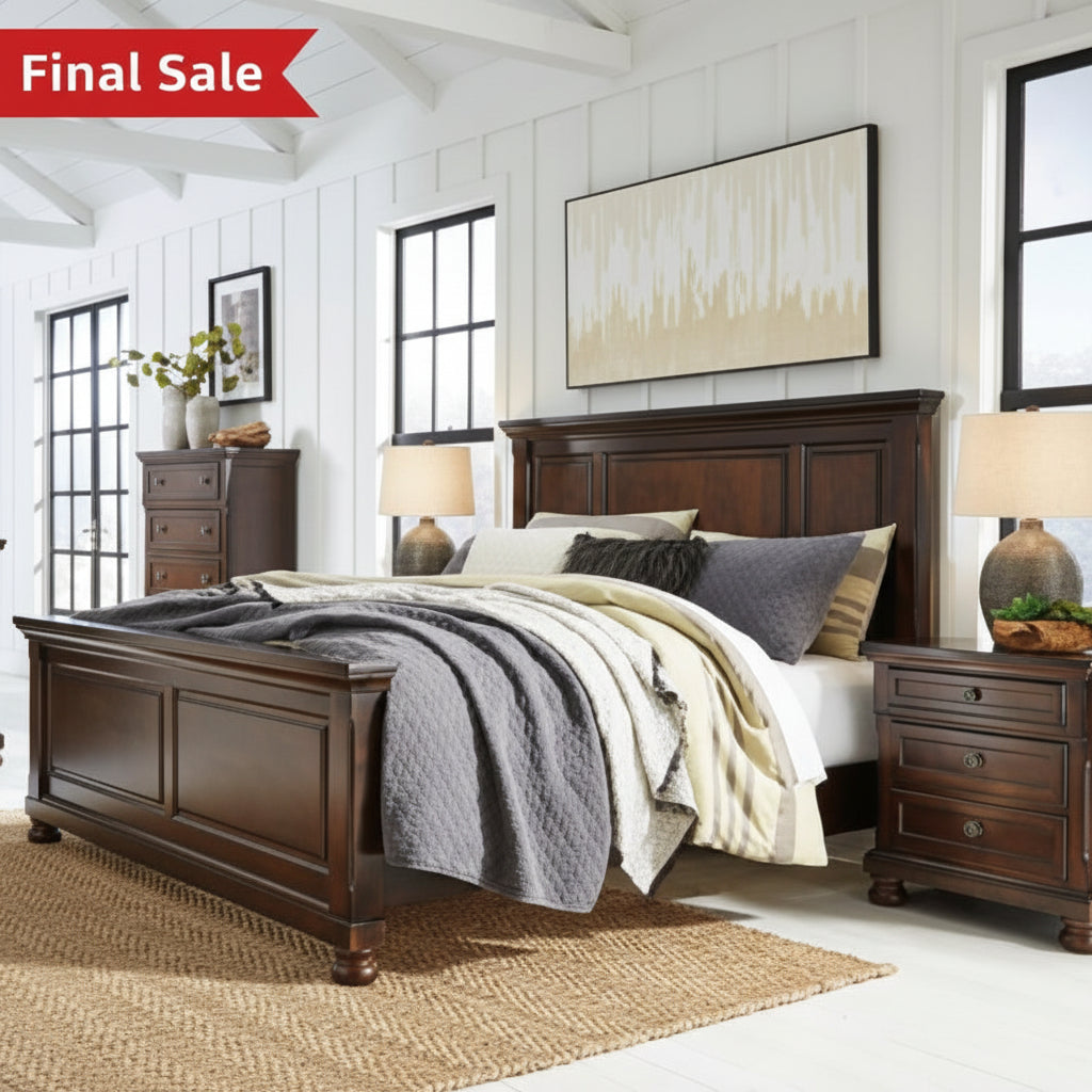 Wooden bedroom furniture set with bed, dressers, and lamps in a room with white walls and large windows.